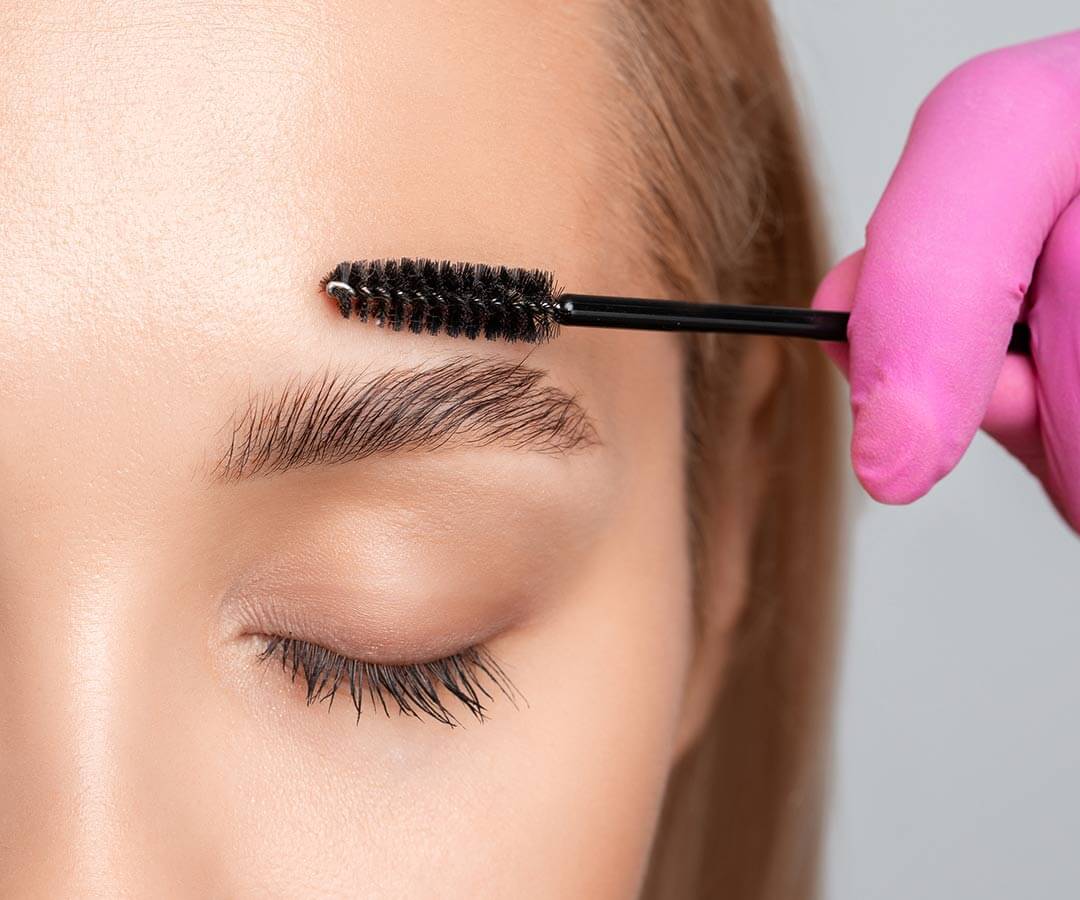 Woman with closed eyes and a mascara brush sitting above her new eyebrow tattoo.