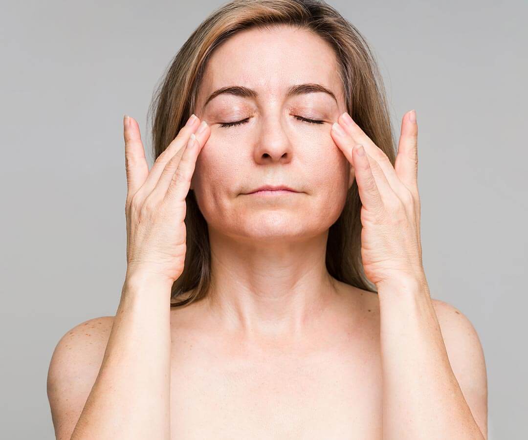 Older woman after medical tattoo treatment with her eyes closed and hands at her temples.